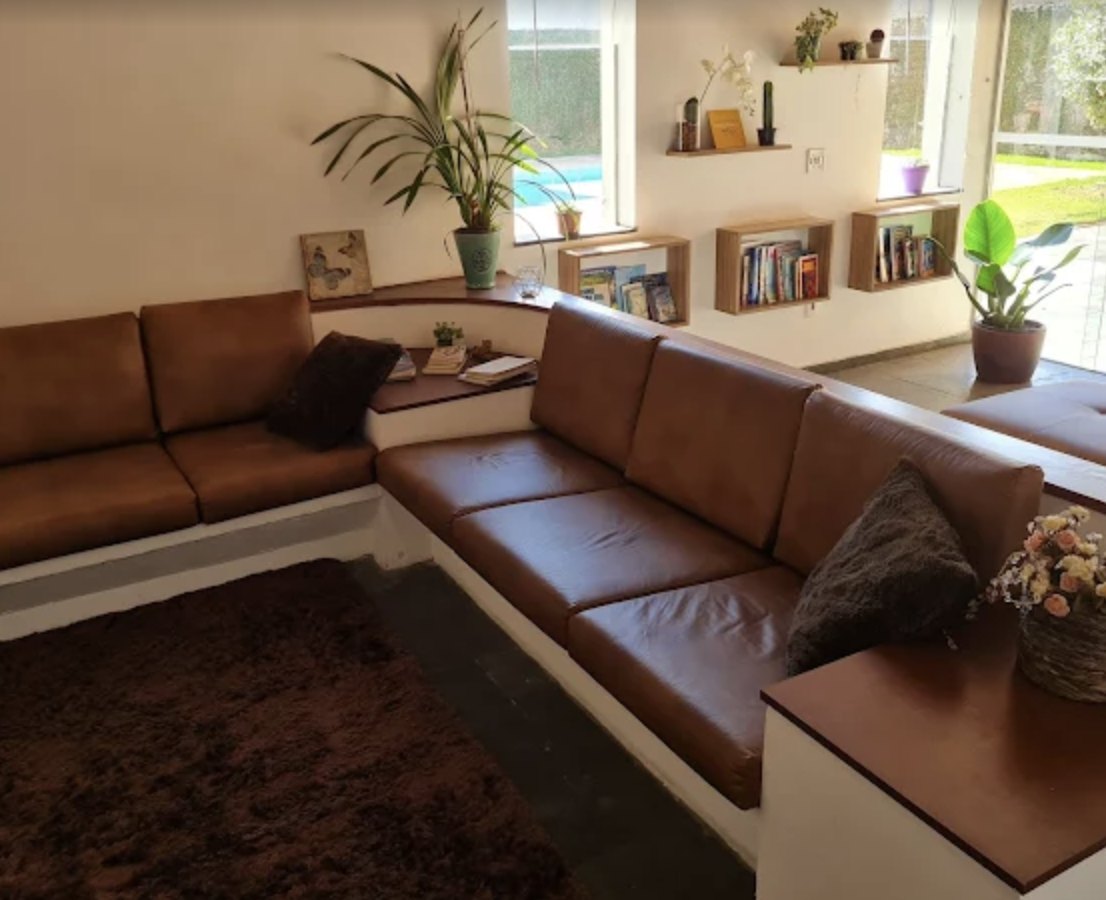 Sala de espera ampla com sofás de couro em L, plantas e nichos com livros